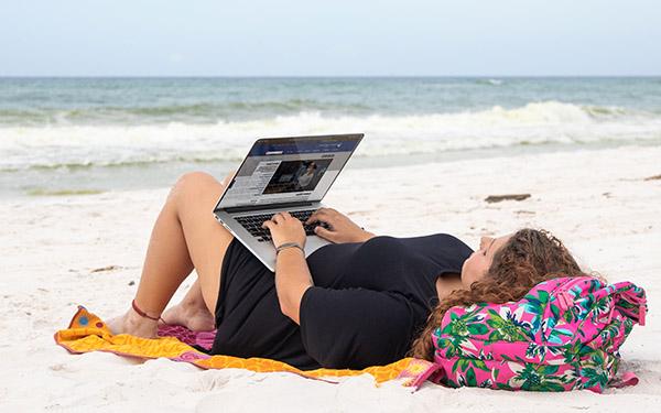一名UWF学生躺在彭萨科拉海滩上使用笔记本电脑.