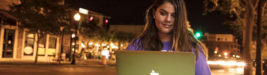 晚上，在彭萨科拉市中心，一位威斯康星大学的学生微笑着使用笔记本电脑.